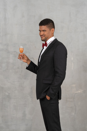 Disgusted-looking young man standing with a glass of champagne