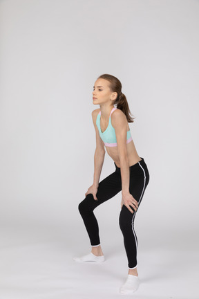 Side view of a teen girl in sportswear squatting and putting hands on hips