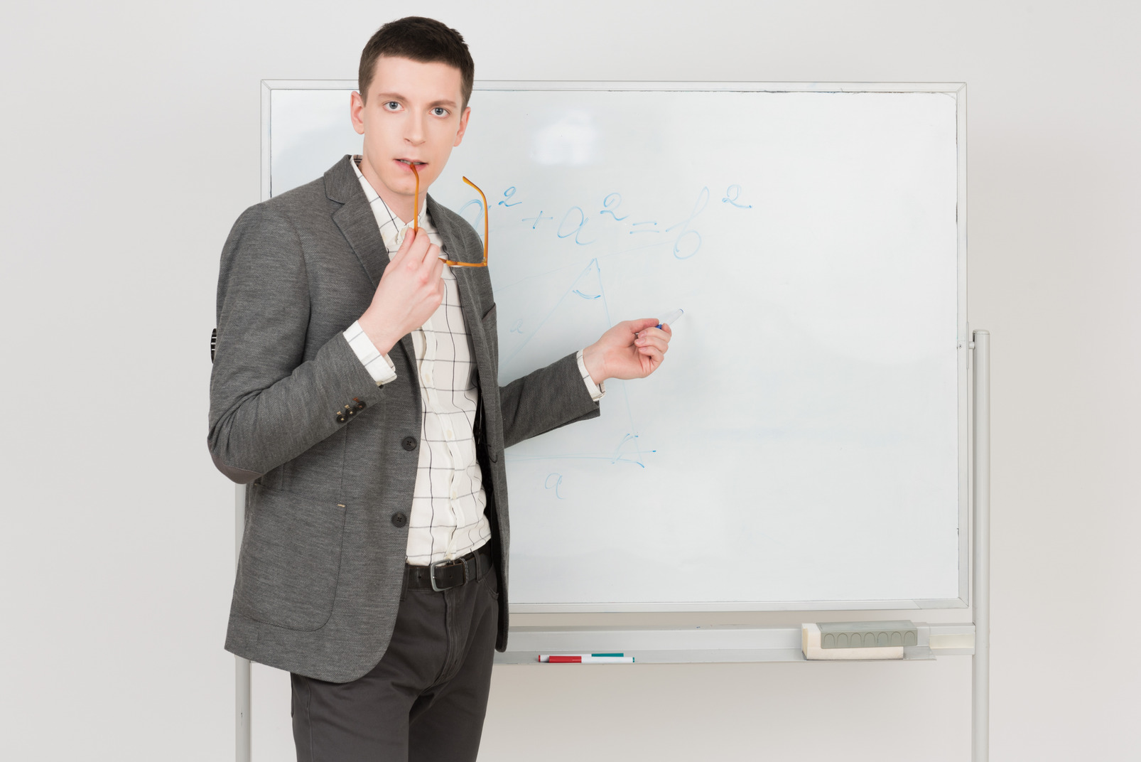 Young attractive teacher pointing with a marker and bitting his glasses