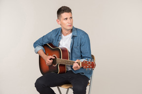 Young guy sitting on the table in profile and playing on guitar