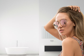 A woman in sunglasses fixing her hair in a bathroom
