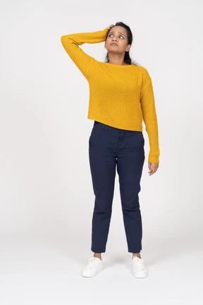Front view of a girl in casual clothes standing with hand on head and looking up