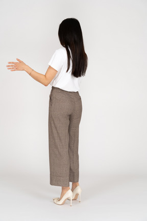 Vista posteriore di tre quarti di una giovane donna in calzoni che alza la mano