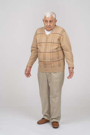 Front view of a confused old man in casual clothes standing with outstretched arms