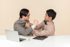 Two young nerds sitting at the table and punching each other into the face