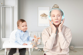 An elderly woman with headphones and a baby in a high chair