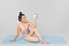 Sonriente joven gimnasta indio sentado en la estera de yoga y sosteniendo una taza de café