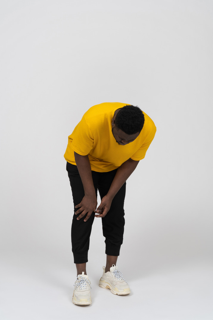 Front view of a dark-skinned man in yellow t-shirt touching his knee