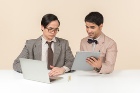 Dois jovens nerds sentado à mesa e usando gadgets