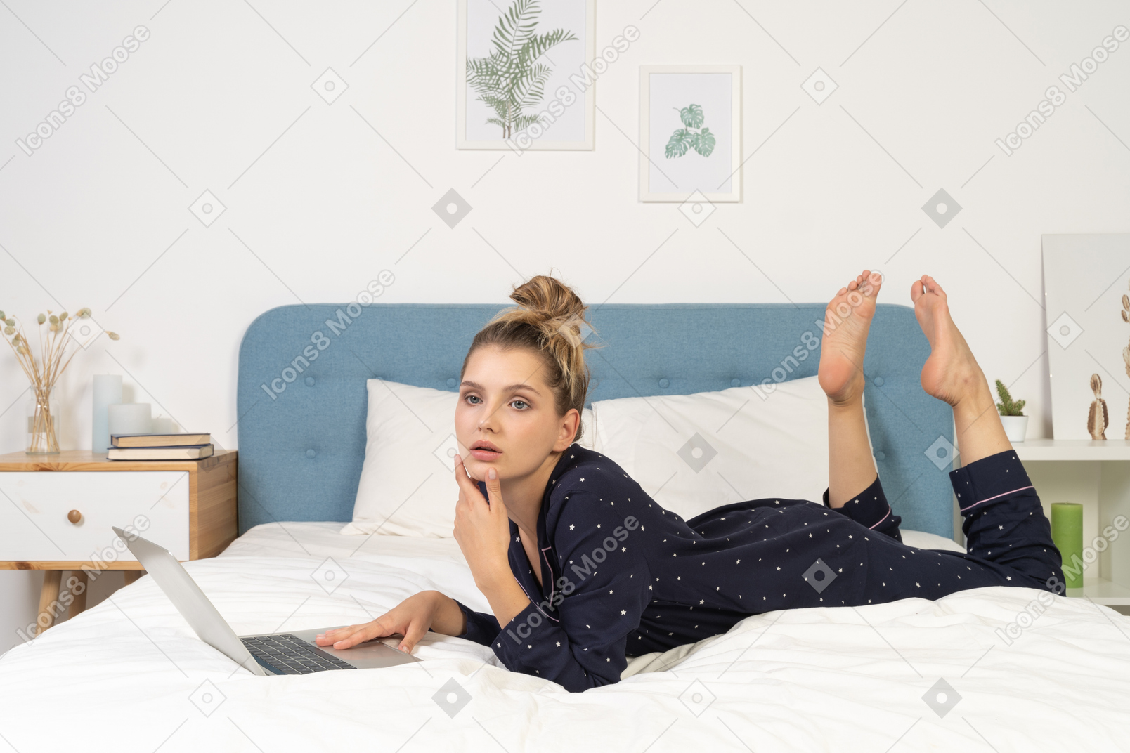 Vista lateral de uma jovem mulher deitada na cama com seu laptop