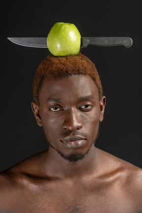 Primo piano un giovane che guarda con fiducia la fotocamera con una mela e un coltello in testa