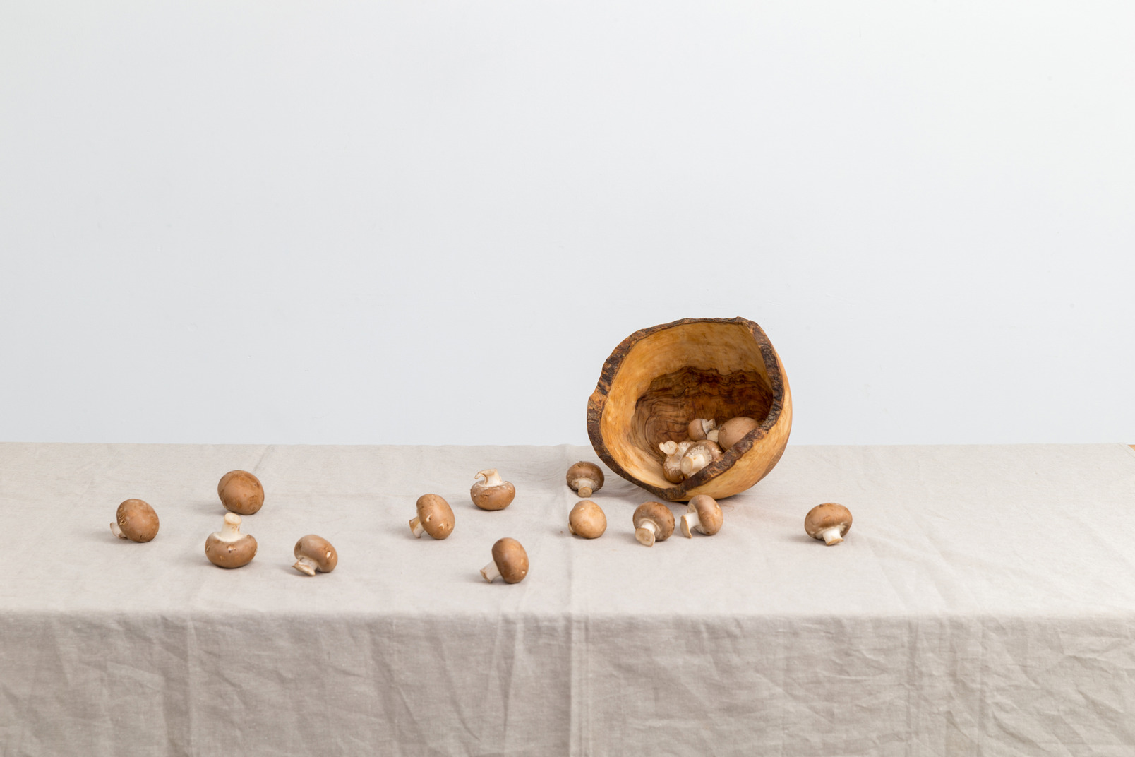 Cogumelos na tigela de madeira e alguns deles jogados na mesa