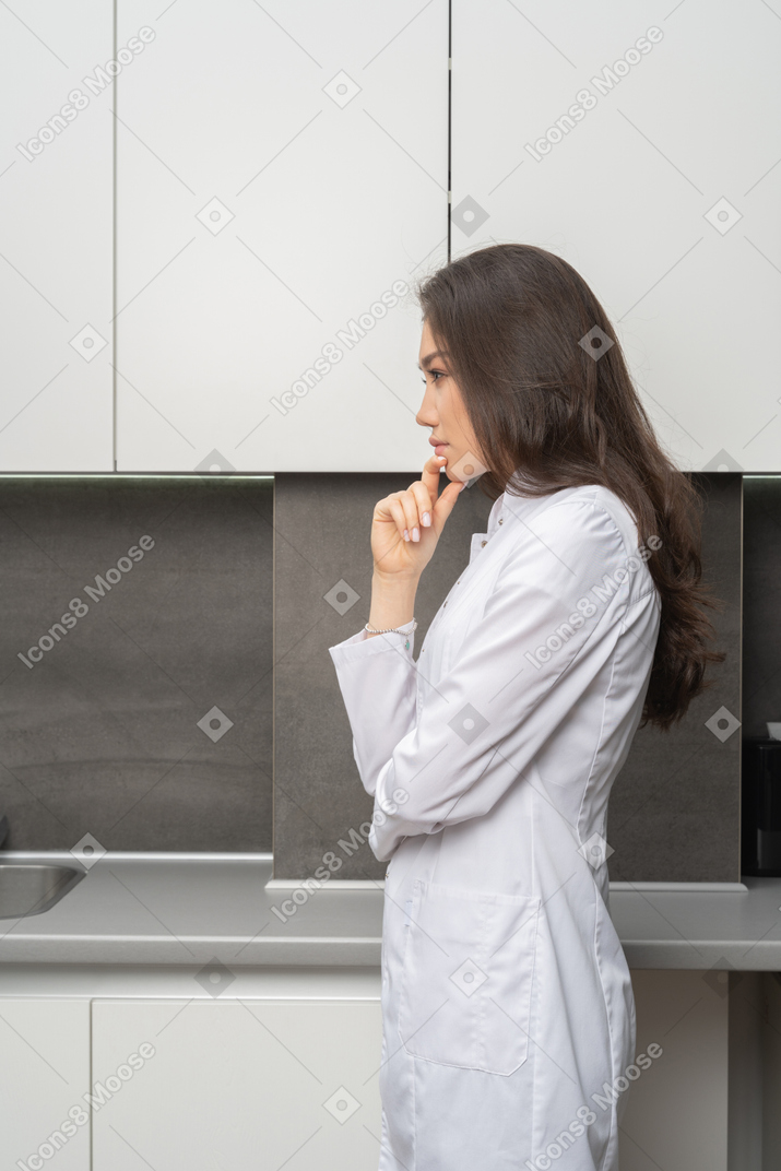 Vista lateral de una doctora dudando tocando la barbilla