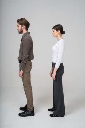 一对年轻夫妇在办公服装站着不动＆眉毛的侧视图