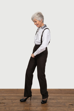 Вид в три четверти шагающей улыбающейся старушки в офисной одежде