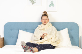 Front view of an ill young lady wrapped in white blanket staying in bed