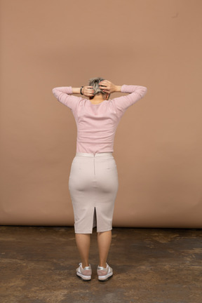 Rear view of a woman in casual clothes standing with hands behind head