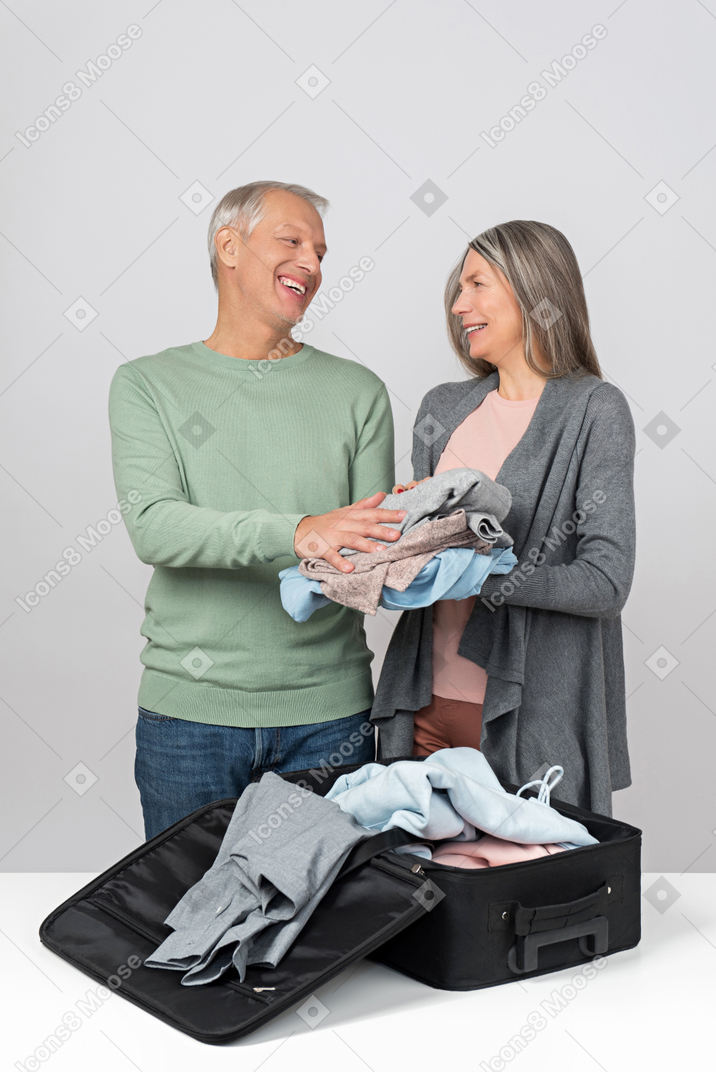 Middle aged couple laughing packing a suitcase