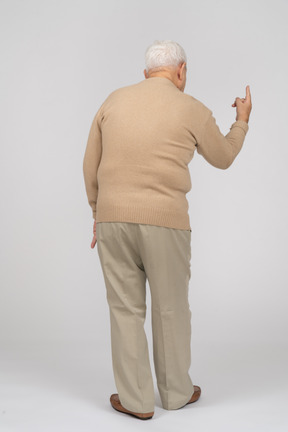 Vista trasera de un anciano con ropa informal apuntando hacia arriba con un dedo