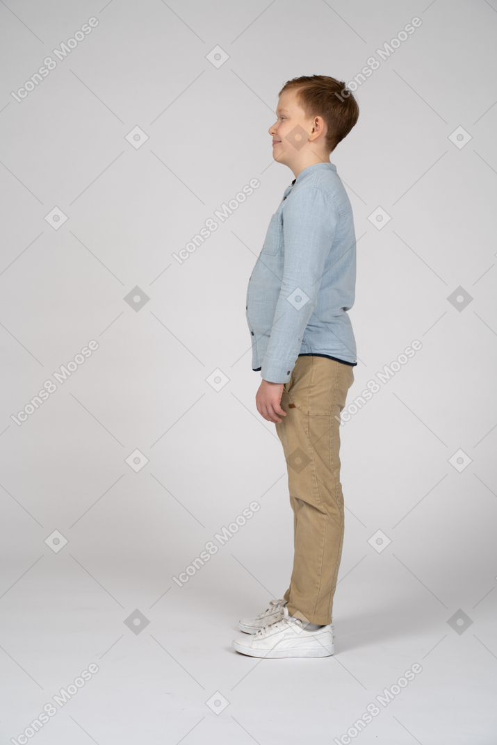 Side view of a boy in casual clothes standing still and making faces