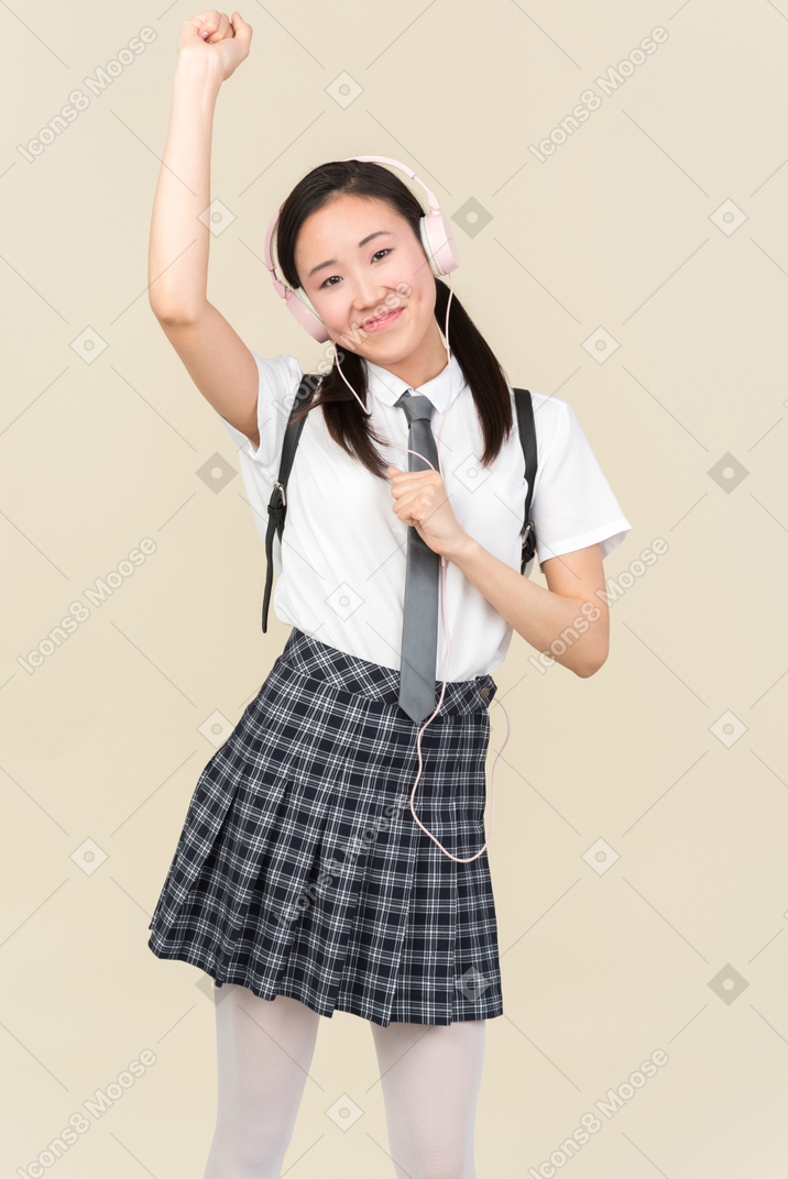 Asian school girl listening to music in headphones and dancing