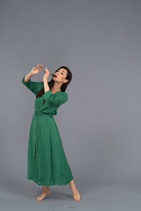 Vista di tre quarti di una giovane donna in abito verde che suona il flauto mentre si appoggia indietro