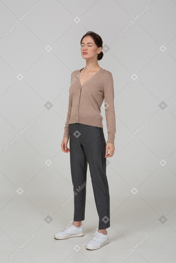 Vista di tre quarti di una giovane donna in pullover e pantaloni in piedi con gli occhi chiusi