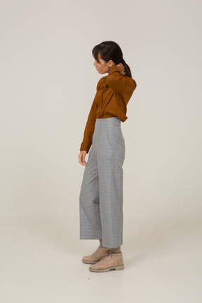 Side view of a young asian female in breeches and blouse touching neck