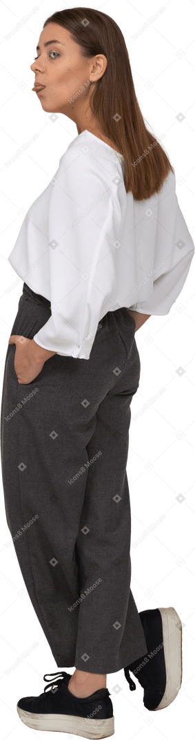 Vue de trois quarts arrière d'une jeune femme en vêtements de bureau mettant les mains dans les poches et montrant la langue