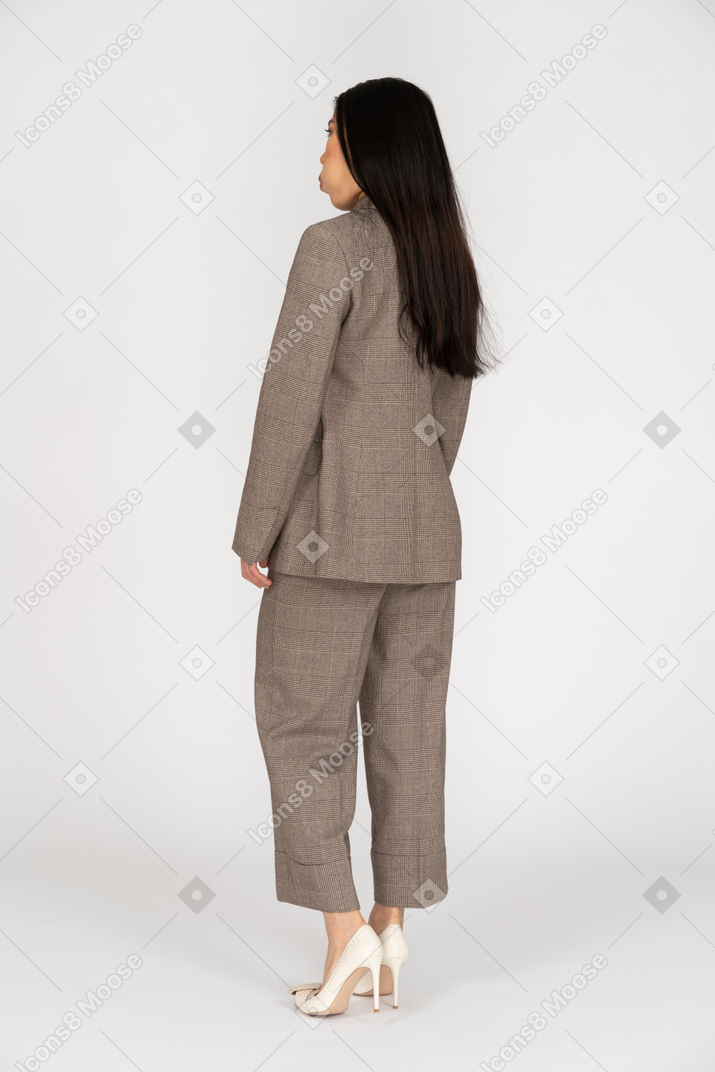 Three-quarter back view of a young lady in brown business suit blowing cheeks