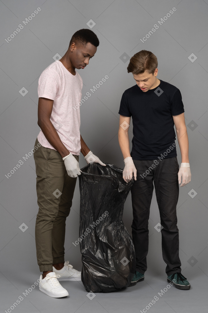 Two young man looking inside a trash bag