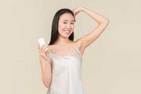 Pretty asian woman applying deodorant on armpit's area