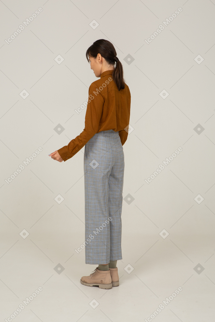 Vista traseira a três quartos de uma jovem fêmea asiática descontente de calça e blusa