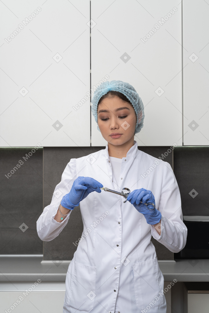 Front view of a female doctor in a medical hat holding a syringe and looking down