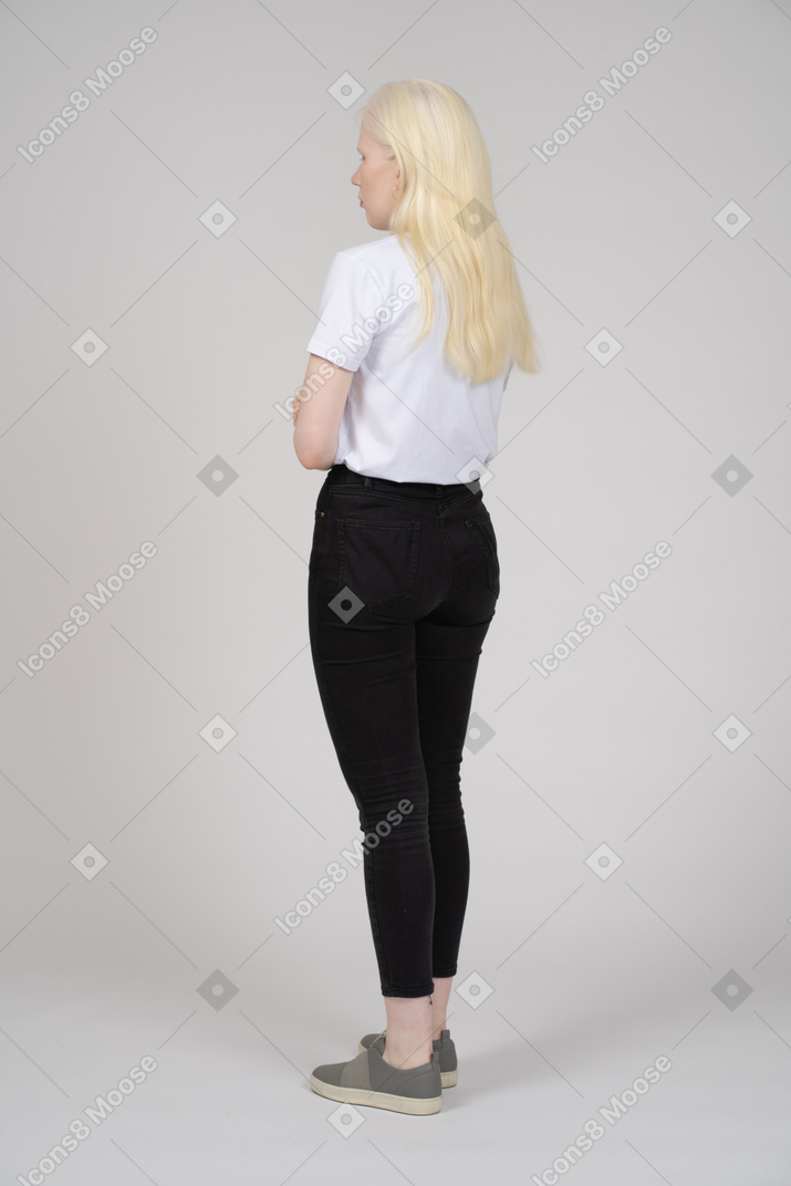 Three-quarter back view of a young blonde woman crossing arms