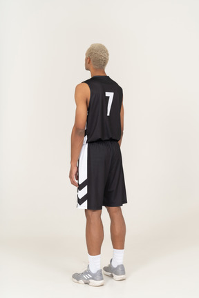 Vista posteriore di tre quarti di un giovane giocatore di basket maschile in piedi immobile