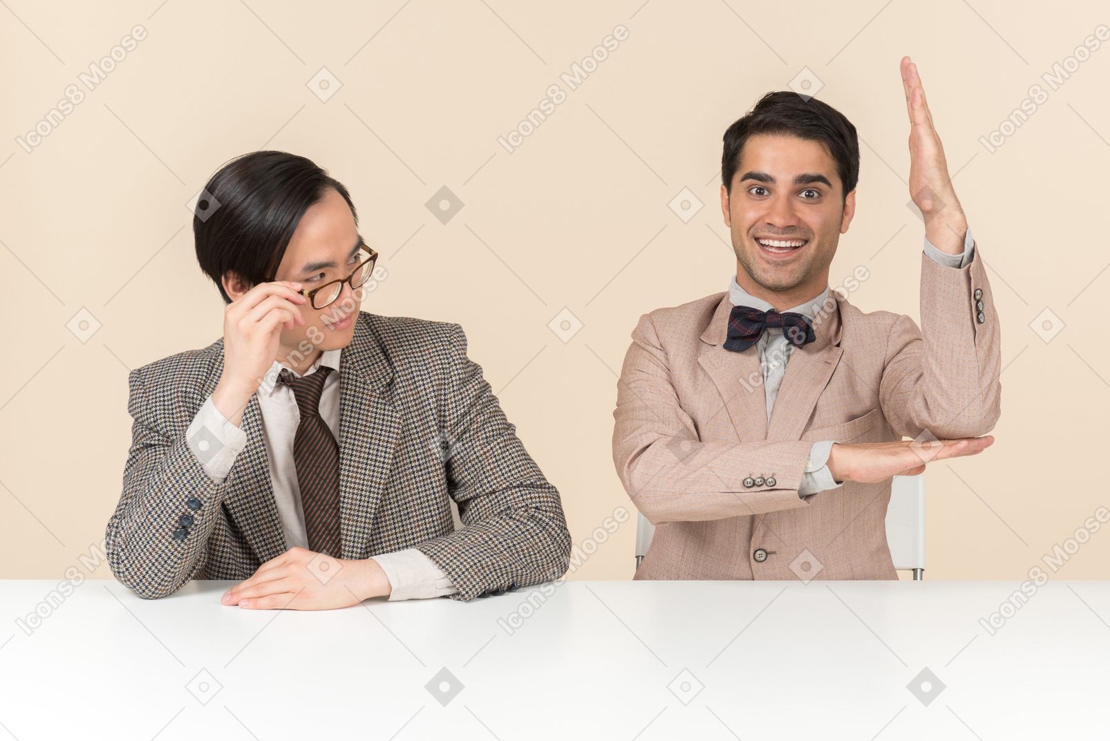 Two young nerds sitting at the table and one of them is raising hand