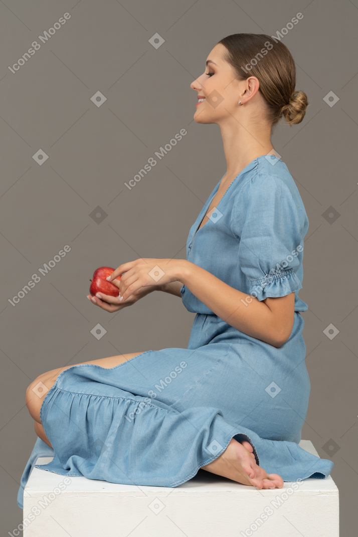 Side view of young woman with apple sitting on cube