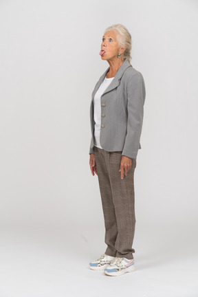 Vista lateral de uma senhora idosa em pé com os braços cruzados e mostrando a língua