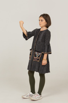 Vista di tre quarti di una bambina in abito che stringe il pugno