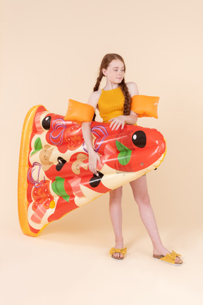 Teenage girl wearing arm floats and holding pizza mattress