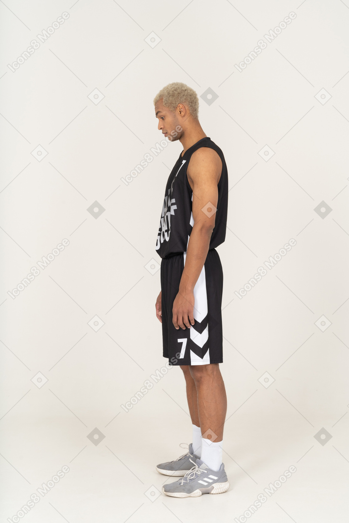 Вид сбоку на молодого баскетболиста, стоящего на месте и смотрящего вниз