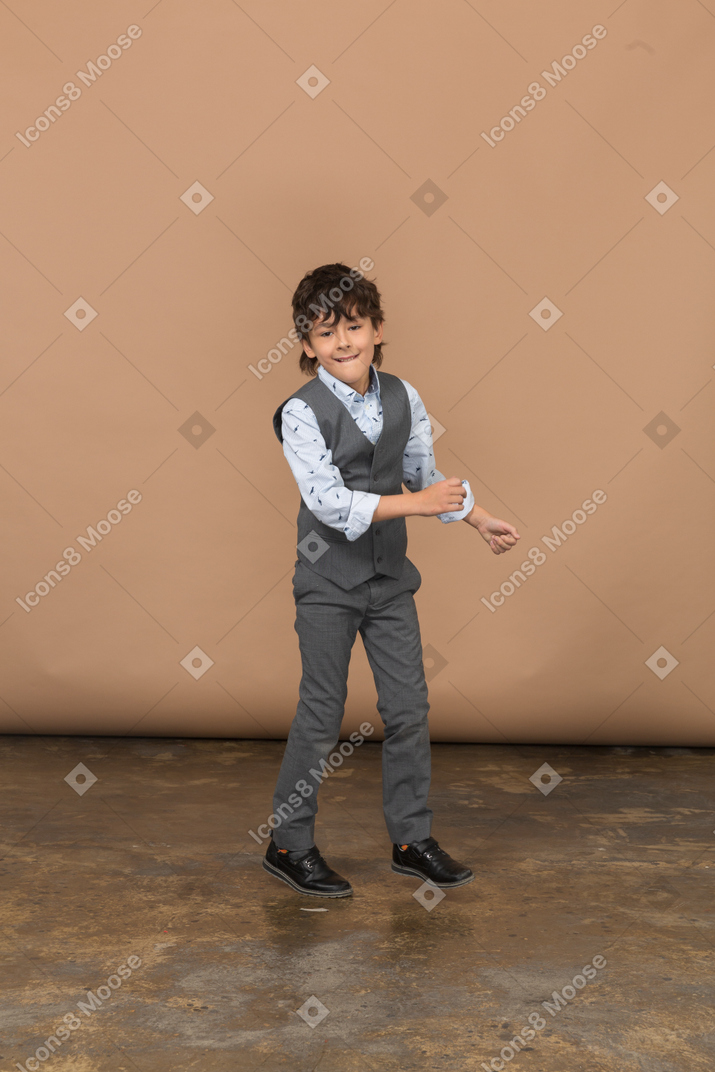 Front view of a happy boy in grey suit dancing