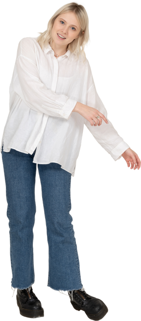 Vista frontal de una mujer rubia en ropa casual haciéndose a un lado mientras extiende las manos y mirando a la cámara