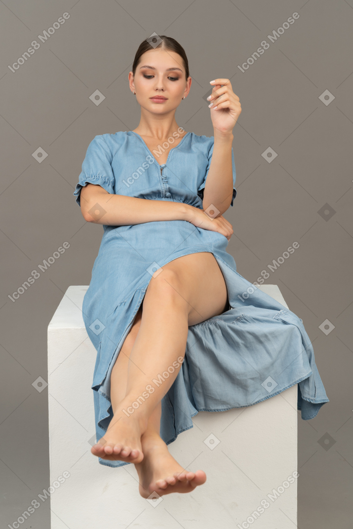 Front view of young woman sitting on cube and looking aside