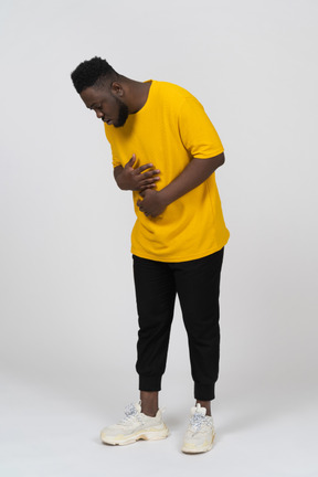 Three-quarter view of a young dark-skinned man in yellow t-shirt touching stomach & looking down