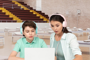 A woman and a boy wearing headphones are looking at a laptop