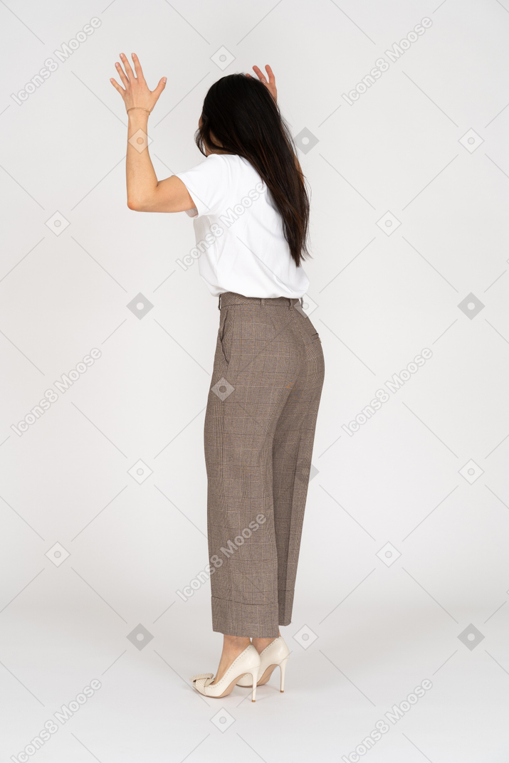 Vista posterior de tres cuartos de una joven loca gritando en pantalones y camiseta levantando sus manos