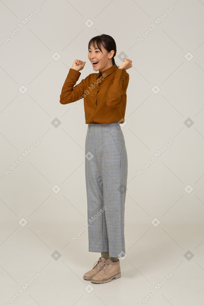 Three-quarter view of a delighted young asian female in breeches and blouse raising hands