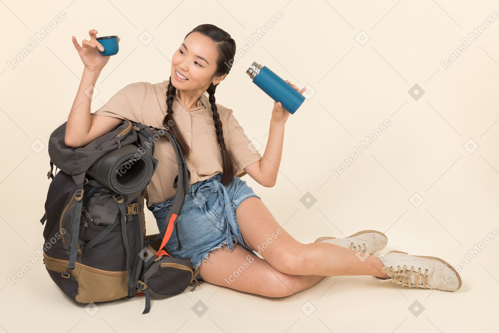 Joven mujer asiática sentada cerca de mochila y sosteniendo termo